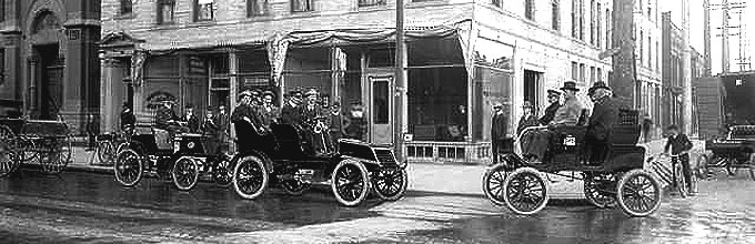 Three automobiles are parked at the corner of 18th (Eighteenth) and Stout streets in downtown Denver, Colorado. Men wearing suits sit in the cars; other men stand on the sidewalk in front of storefronts including: Colorado Winton Motor Carriage Company and the Bicycle Supply Company (1761 Stout) and the Schuster & Larimer Plumbing Company (1759 Stout). The awnings of the businesses are tied back. Street scene includes: a young boy on a bicycle, another holds a bicycle tire, and a man sits in the back of a parked truck. A woman peers from behind a curtain in a third-floor, arched window above the Winton Motor Car office.  Date [1902?]  Photograph by Joseph Collier.
Title: Cars in downtown Denver.  Call Number: C-2.   
URL - http://gowest.coalliance.org/cgi-bin/imager?00130002+C-2

Hyperlink to Denver Public Library.