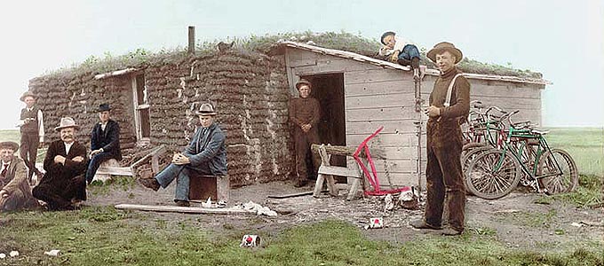 Photo: Christ Nelson sod house, Soper Post Office, North Dakota, 1896. Sod house with a wooden lean-to, stovepipe and one window showing. Five bicycles are against the side of the addition. Eight people in the foreground from left to right: George Bakken, Edwin Gjevre, John A. Lind, Thomas Haugen, Christ O. Nelson (owner), John Erickson, Herman Haugen (on the roof), Martin Erickson. There are also saw horses, a shoe on the roof, and tin cans and trash on the ground.

Fred Hultstrand History in Pictures Collection, NDIRS-NDSU, Fargo, ND.  DIGITAL ID: (hand-colored) ndfahult c080.  Photographer: John McCarthy. Gift: Donna Jean Verwest, 1969.  Library of Congress
