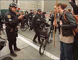Outside the Convention Center, Seattle Police Officer B. Conway issues a warning to Rozl after being hit by the protester's pole, which sported a giant wooden butterfly at the end. (November 29, 1999)

Photo Credit: Robin Layton/Seattle Post-Intelligencer